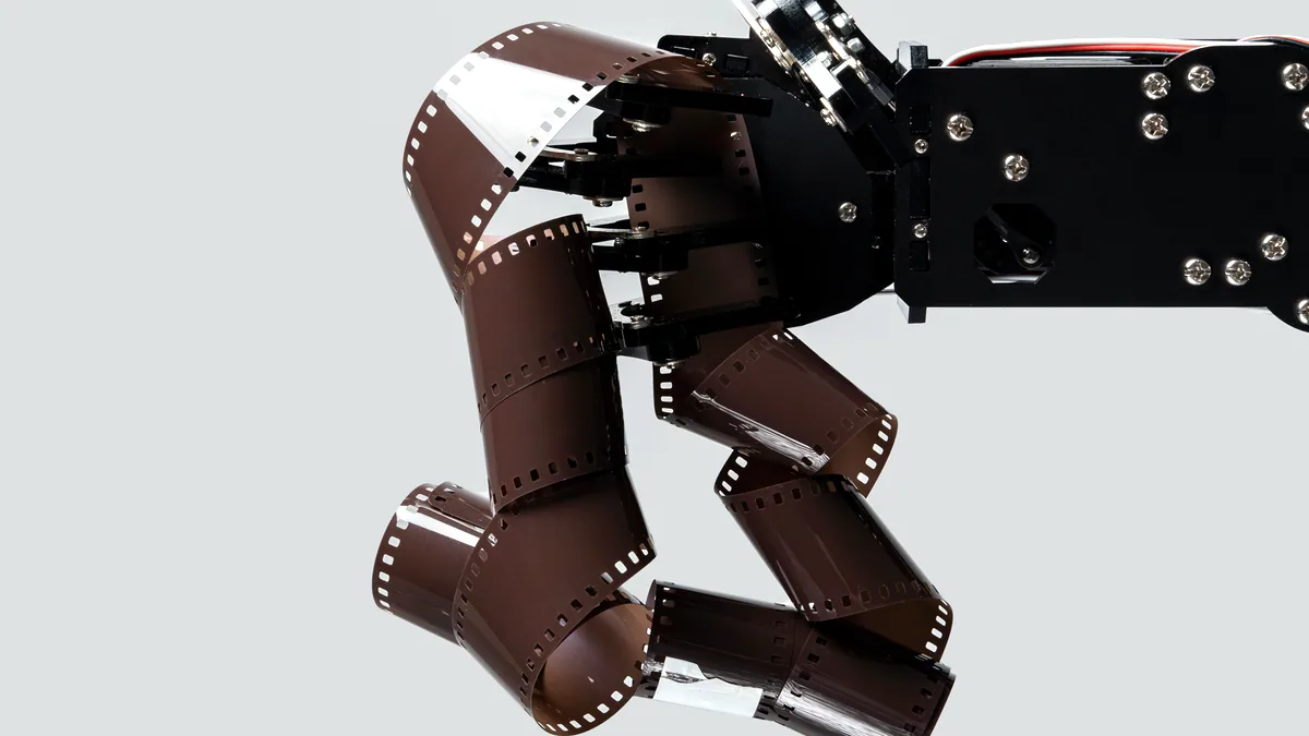 A polished metal hand reaching toward a brass film reel.