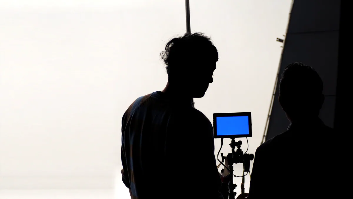 A silhouette in a chair before a bright monitor on set.