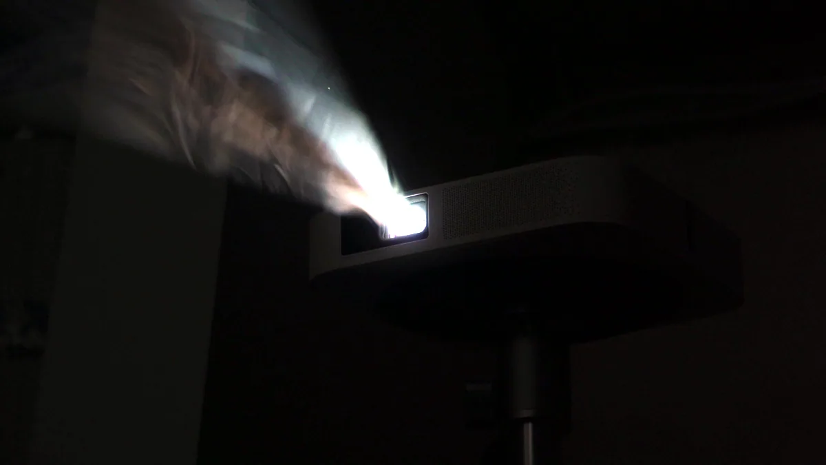 A projector lens throwing a beam of light into a dark room.