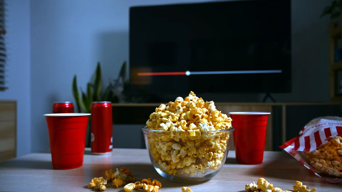 A bowl of popcorn and a remote on a dark sofa.